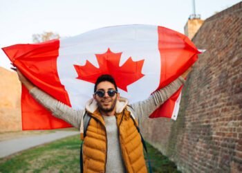 Young handsome man waving Canadian flag outside in the park