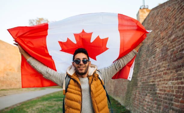 Young handsome man waving Canadian flag outside in the park
