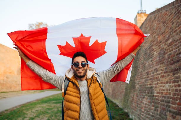 Young handsome man waving Canadian flag outside in the park